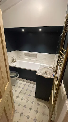 Bathroom with navy walls, marble bath surround, mosaic floor tiles and gold heated towel rail
